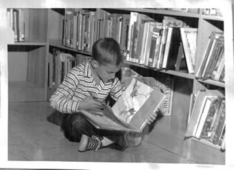 Black and white photo of a young boy reading during Picture Book Time at the Melville Library