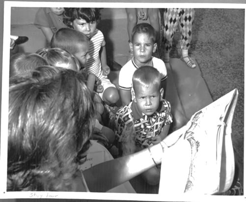 Black and white image of children during story hour on the front lawn.