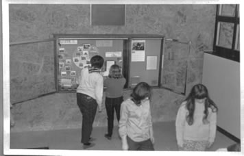 Black and white image of the senior girl scouts helping with an exhibit in the lobby of the Dix Hills building
