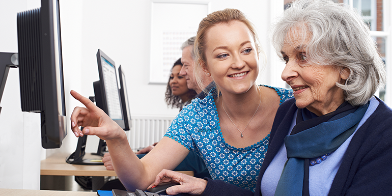Younger woman helping older woman on a desktop computer