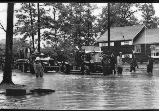 Black and white photo of firefighters standing in flood waters