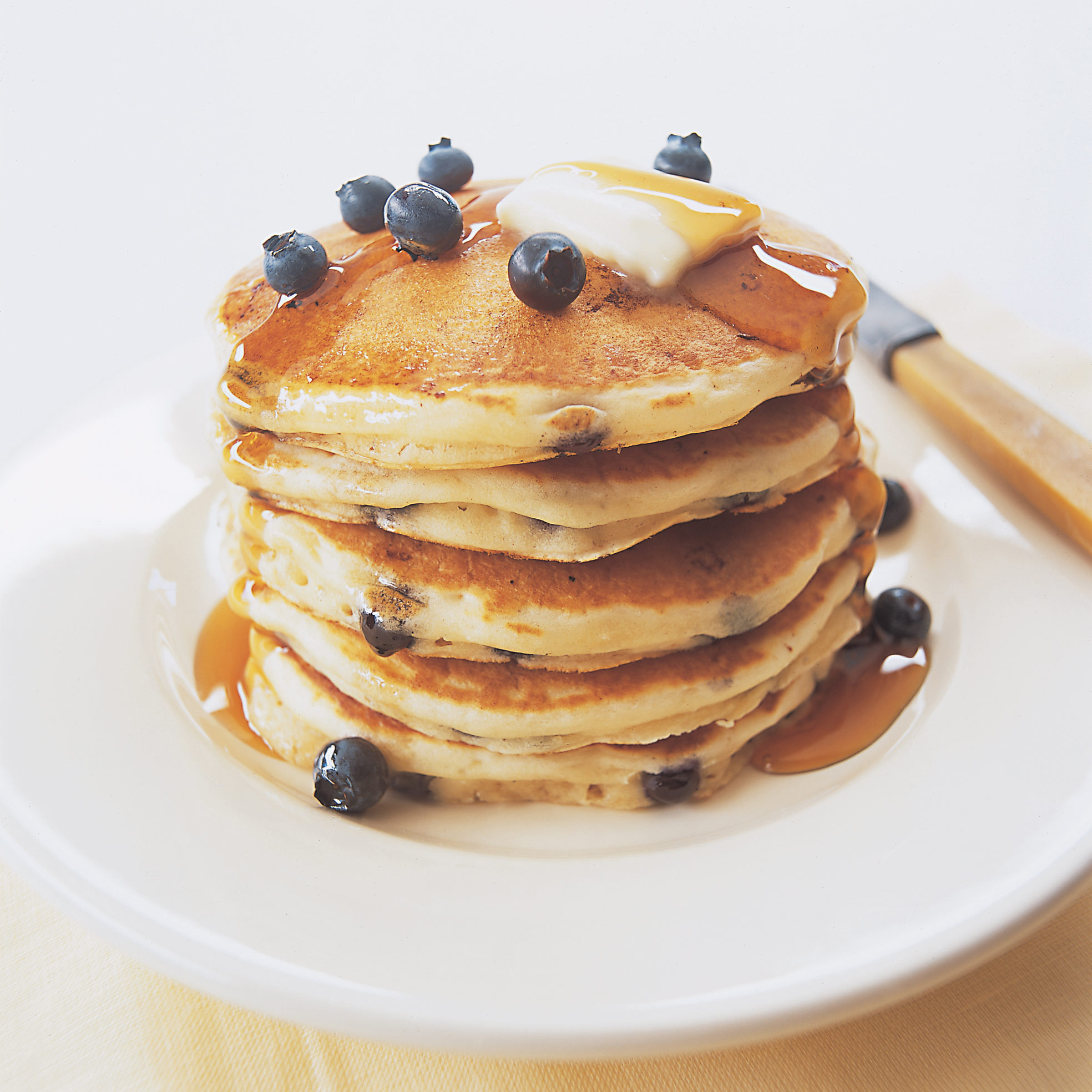 Stack of blueberry pancakes, fresh blueberries on top with butter and syrup. 