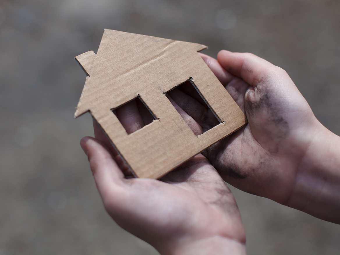 Image of a person with dirty hands holding a cardboard cut out of a house. 