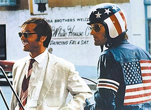 Two men facing left, one wearing American emblems and a helmet, the other in a white suit.