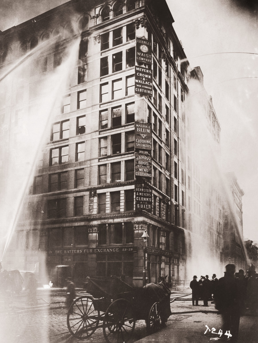 Black and white image of the old building in NYC that housed the shirtwaist factory. It shows the smoke coming out of the windows and the water being sprayed from fire hoses onto the building from the street.