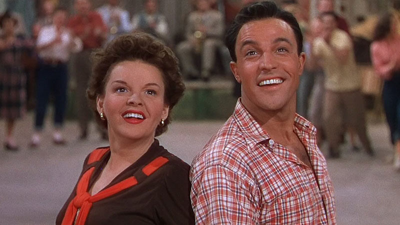 Photo of Judy Garland and Gene Kelly from the musical "Summer Stock". They are standing almost back to back facing the audience, both with a big smile. 