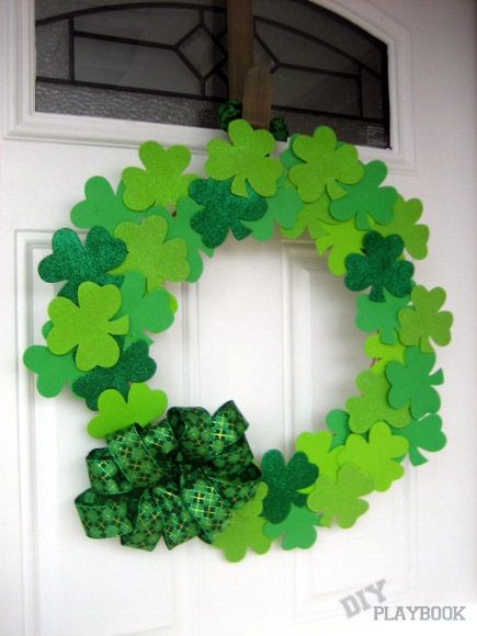 Image of a wreath made with shamrocks cut out of foam in different shades of green. A big green bow is on the bottom of the wreath.