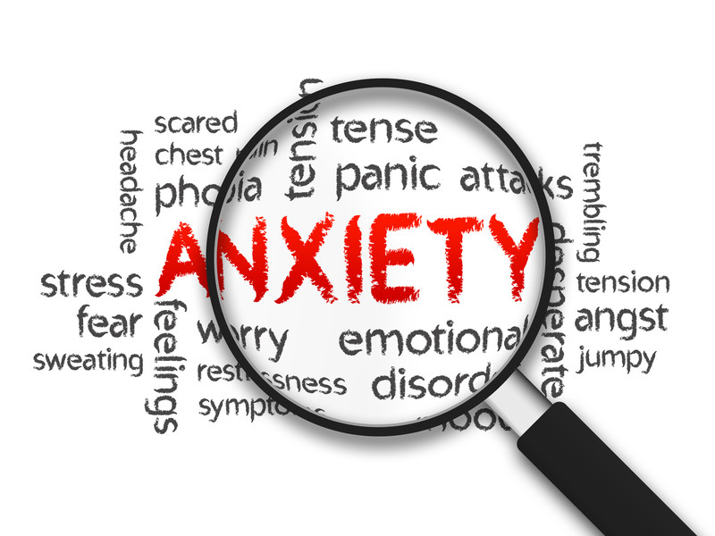 The word Anxiety written in red under a magnifying glass with symptoms of anxiety spelled out  in words. For example, the words "panic attack", "Worry", "Tension",  "chest pain" etc.  