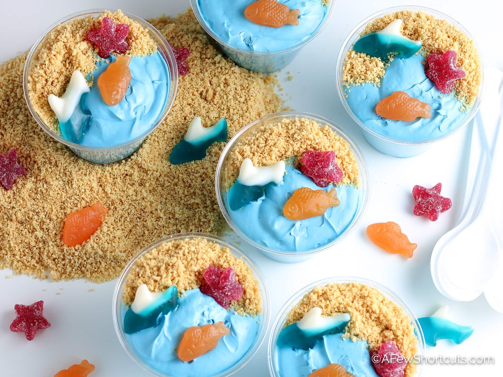 image of 6 blue pudding cups with graham cracker sand and gummy fish on top of them.