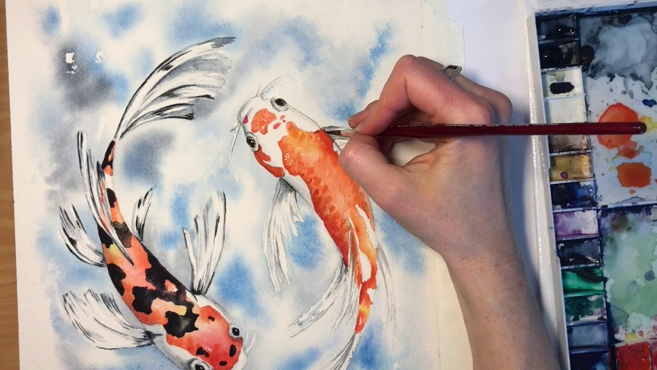 image of someone's right hand painting orange koi fish with a set of watercolors beside the hand.