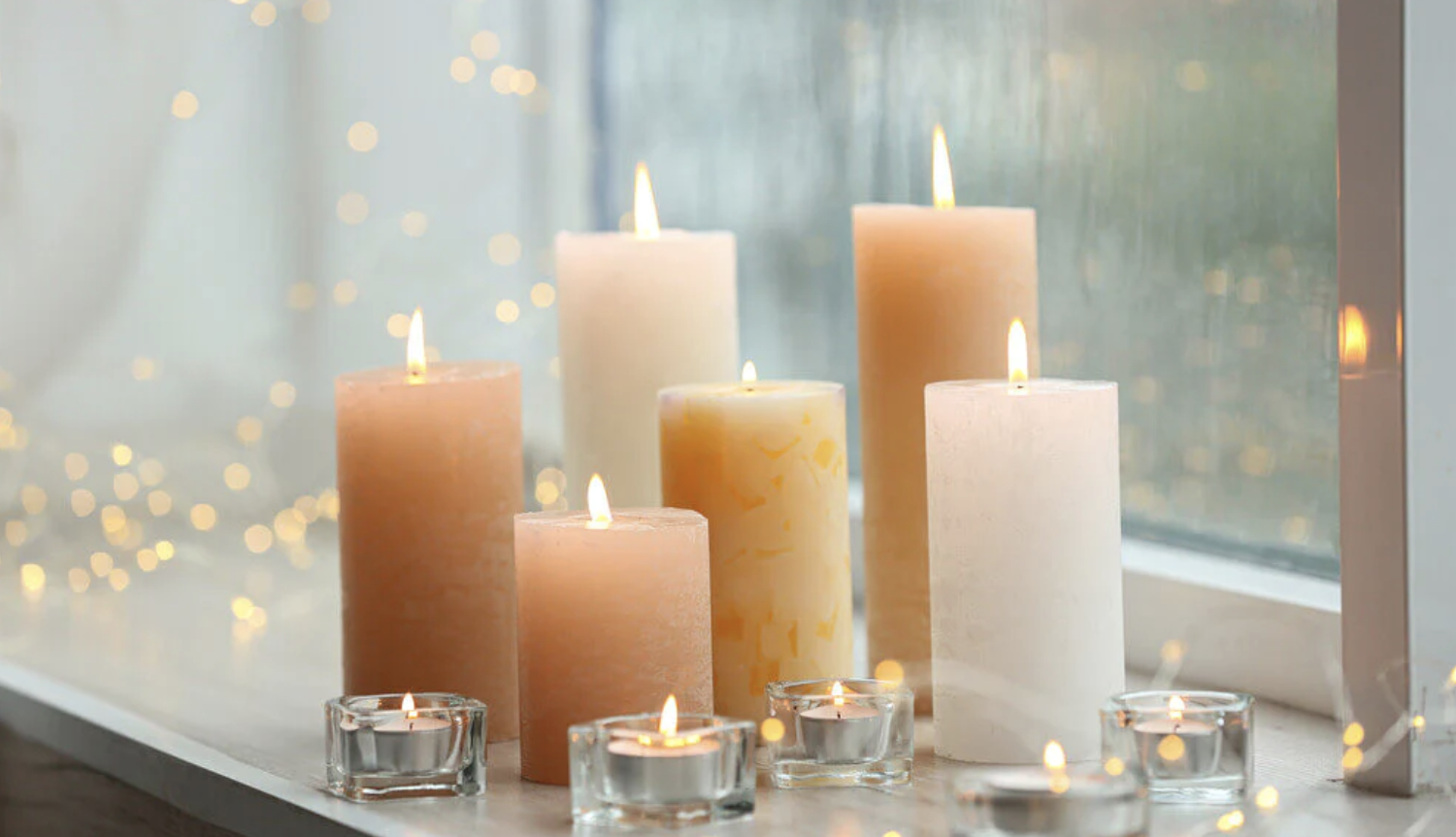 Image of 6 tall orange and white lit candles and 5 smaller tea light candles in front of a window.