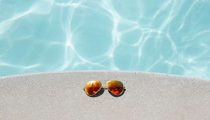 image of a stone ledge over a pool with tinted sunglasses resting on top of it.
