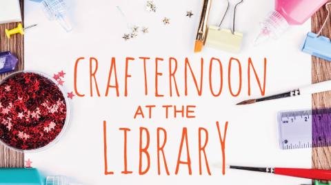 Image of a piece of paper on a table with the words "Crafternoon at the Library" written in orange and all capital letters. Around it are glittery stars strewn on the paper and table, a purple ruler, various colored paint crushes and paints and craft materials. 