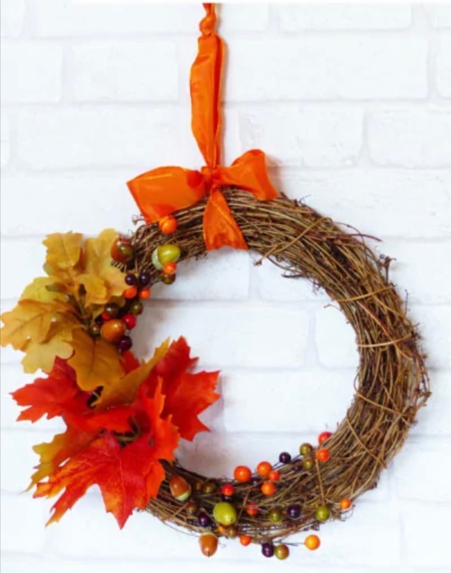 Image of a wreath made with straw, artificial leaves and berries. 
