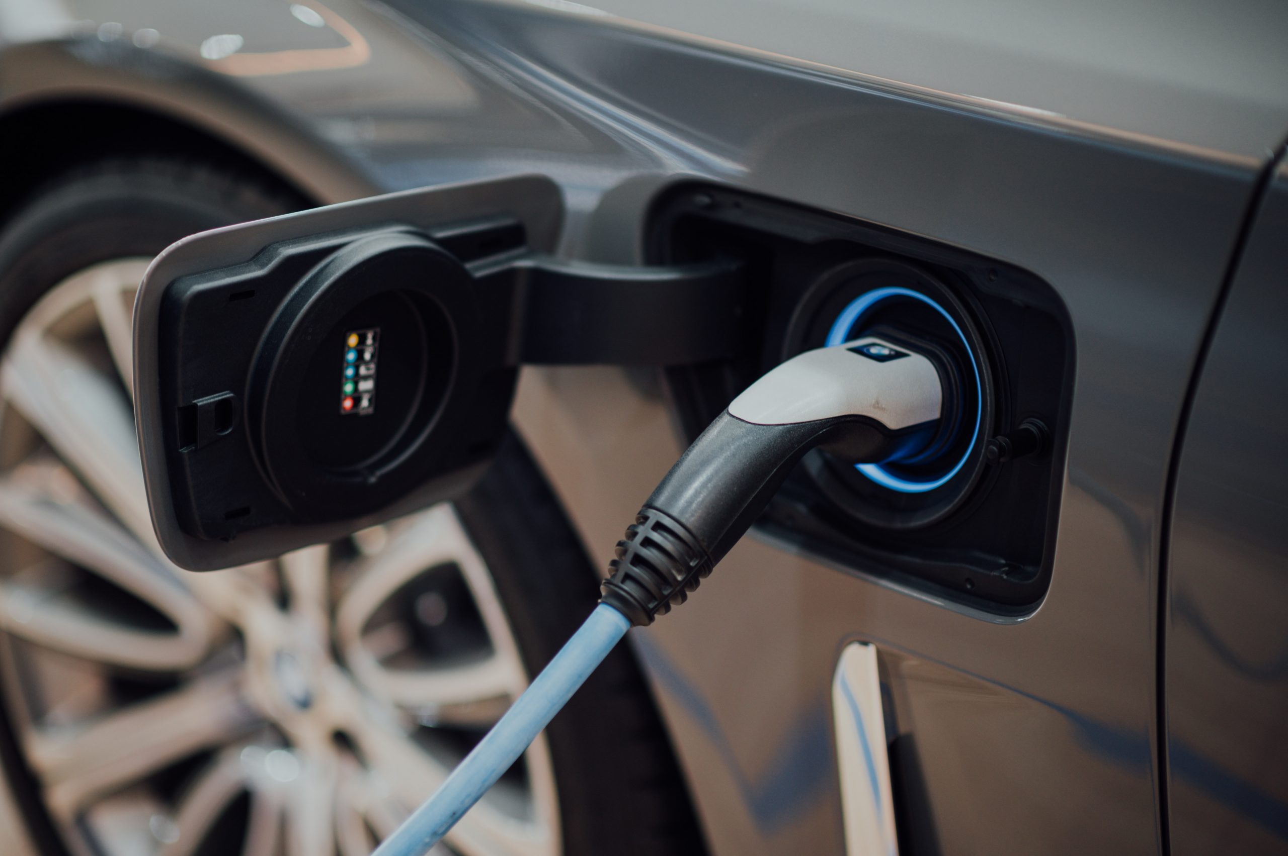 Image of a portion of a silver car with focus on an electric car charger plugged into the slot on the car. 