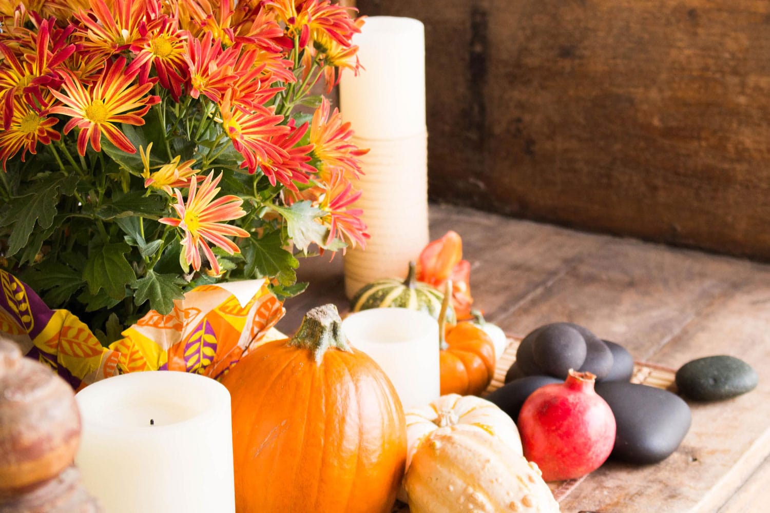 Image of spa stones, a pomegranate, pumpkins and squashes, candles, and orange flowers on a wooden floor.
