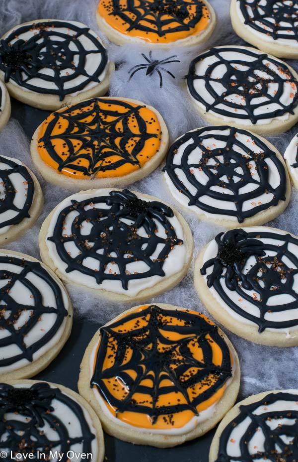 Image of sugar cookies with white and orange icing and a black spiderweb on them