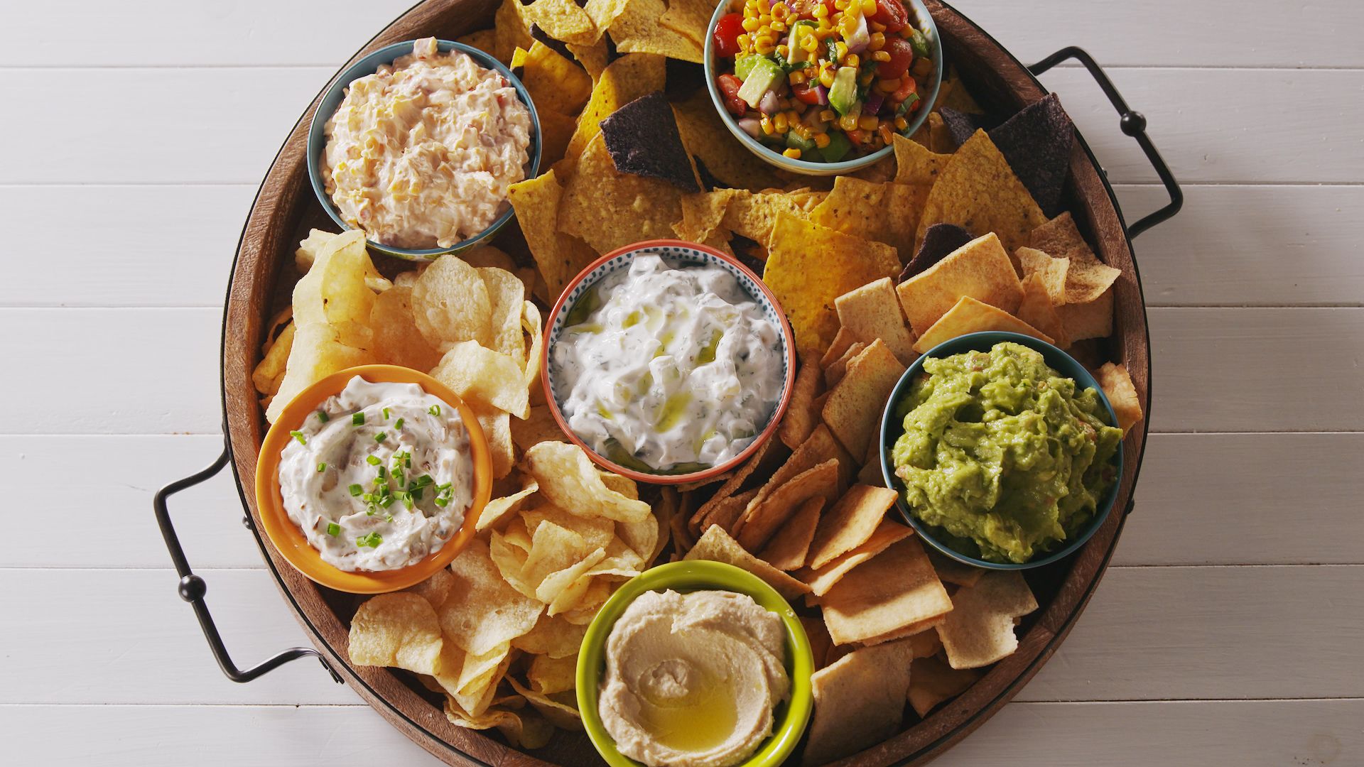 Image of a bowl of chips with 5 different dips on top.