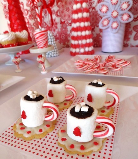 Image of cookies with a marshmallow on top on a tray. The cookie looks like a saucer and the large marshmallow with chocolate icing and candy cane handle make it look like a cup of hot chocolate.