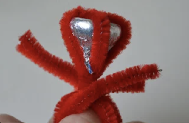 Image of a Kiss Ring, which is a red pipe cleaner wrapped around a silver Hershey's Kiss on someone's finger.