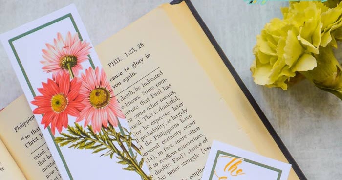 Image of an open book with a bookmark in it; the bookmark has pink flowers on a white background, and a blue border, and next to the book are yellow flowers laying to the side.