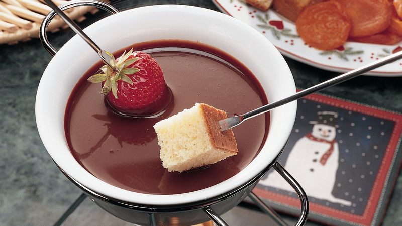 Image of a white bowl filled with chocolate fondue, a metal skewer dipping a strawberry and cake into it.