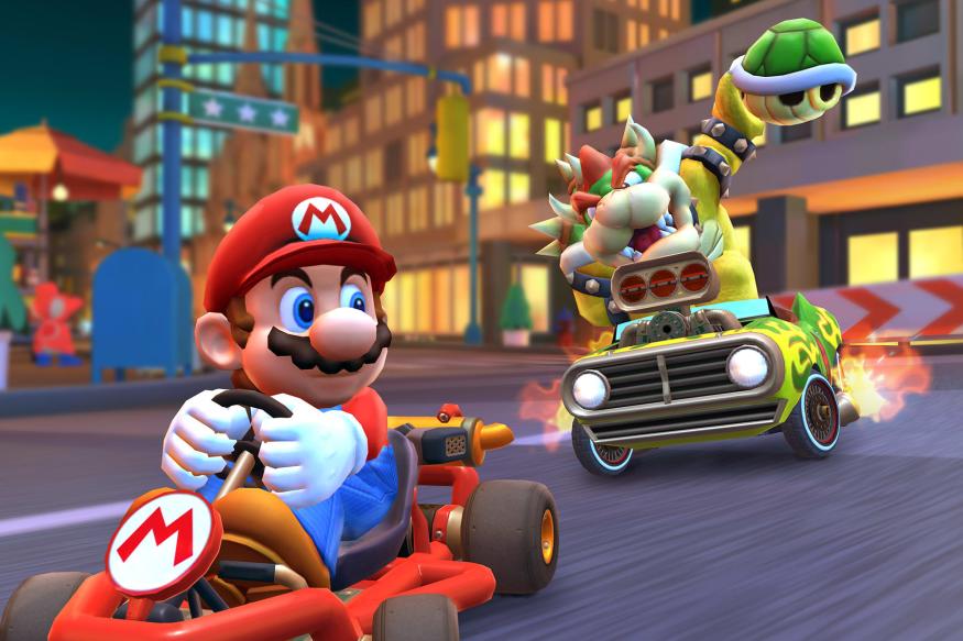Image of Bowser from Mario Kart winding up to hit Mario with a green shell from behind on a road with city buildings in the background.