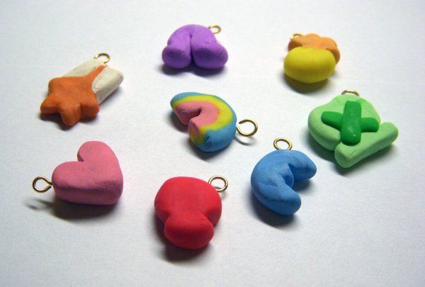 Image of 8 multicolored sculpey charms laid on a white table in the shape of Lucky Charms marshamllows with little rings embedded in the tops of each.