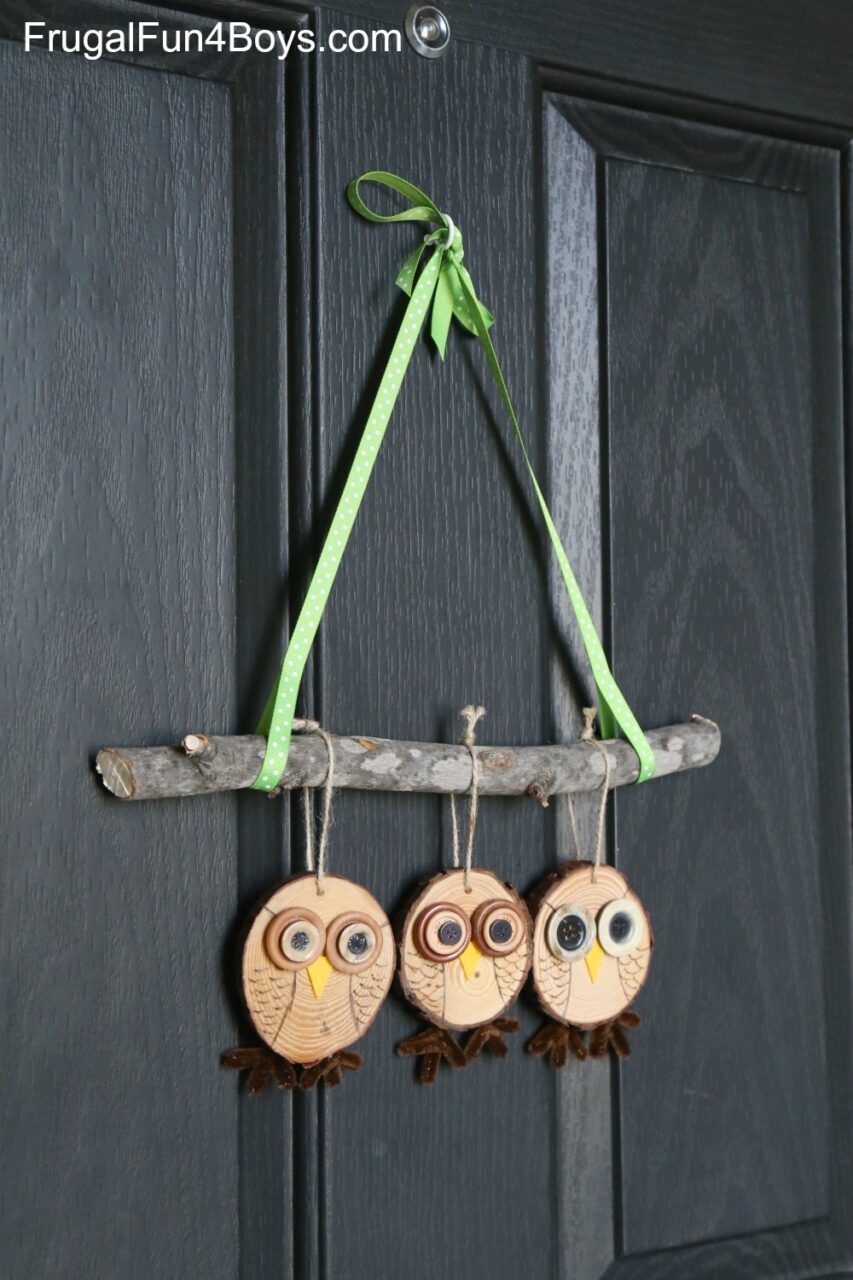 Image of the craft featuring a stick with 3 round pieces of wood hanging. The round pieces of wood are decorated to look like owls. 