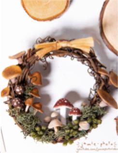 Wreath with fake lichen and mushrooms on it with an orange bow on top.