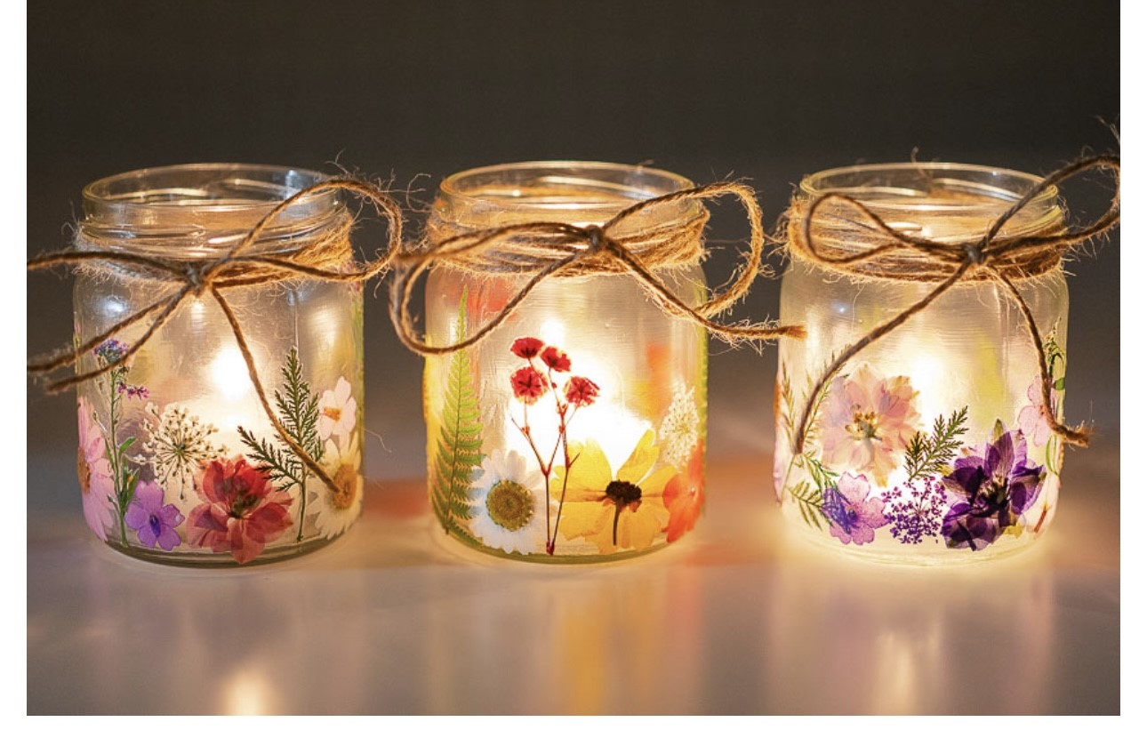 Image of the craft featuring mason jars with a tea light non flammable candle inside. Pressed flowers decorating the jar and a twine bow on the jar lip.