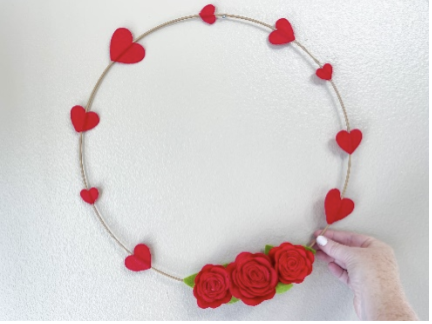 Wire wreath being held by one manicured hand covered in hearts and roses.