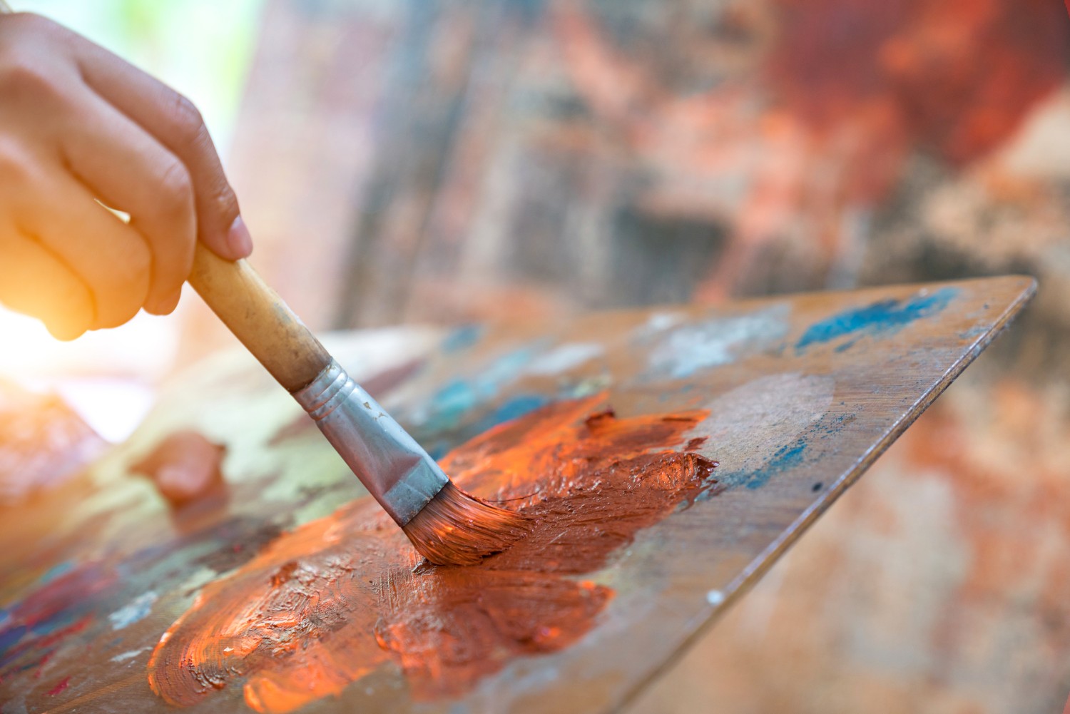 Paintbrush running along a canvas, held gently with brown and orange paint smearing from it.