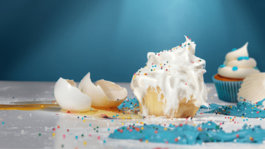 Cupcake and broken egg and blue frosting on a counter over a blue background