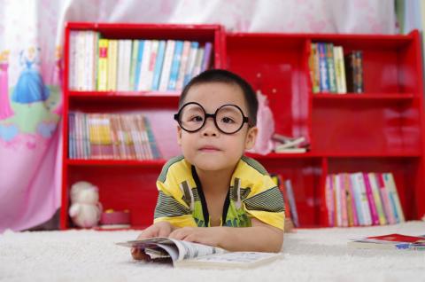 Young child wearing glasses sitting in front of a red bookshelf