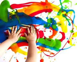 Child with both hands smearing multi colored paint around a paper. 