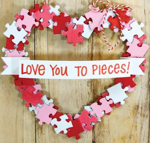 Heart wreath made out of red, pink and white puzzle pieces with a ribbon that states :love you to pieces"