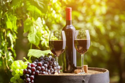 A photo of a bottle of wine with 2 glasses and a bunch of green and a bunch of red grapes. 