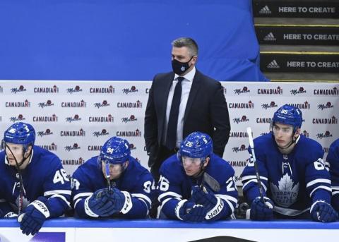 Photograph of hockey team members along side the ice rink in their gear and their coach wearing a cloth face mask. 
