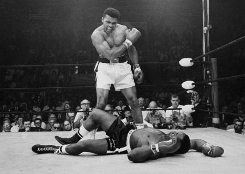 Photograph of Mohammed Ali in the boxing ring with his opponent on the floor of the ring. 