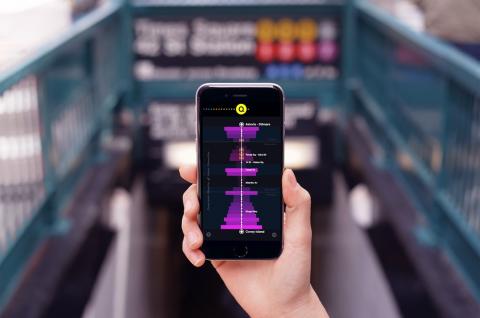 Image of hand holding up a phone with a travel app on it in front of a subway station