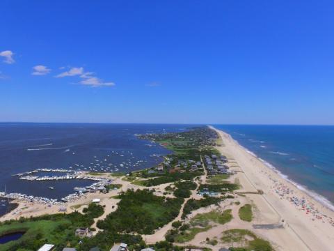Aerial view of a Fire Island, showing a sandy beach with greenery on the left and an ocean surrounding it.
