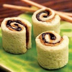Image of little peanut butter and jelly rolls that look like sushi on a plate. 