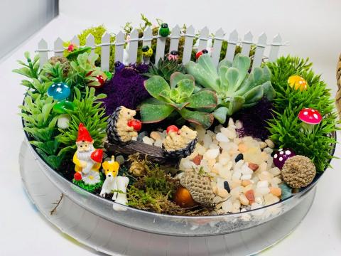Image of a terrarium. Succulent plants in a bowl with little gnome and fence decorations..