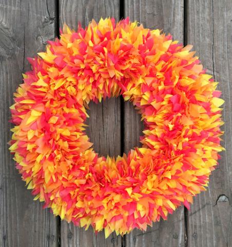 Image of a circle wreath with red, yellow and orange leaf like poofs. 