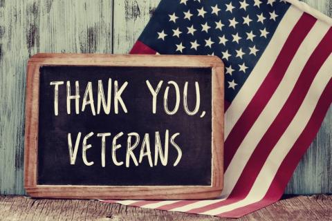 Image of a little chalkboard with the words thank you veterans spelled out and an American flag behind it. 