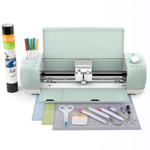 Image of a Cricut Machine with supplies to use like scissors, markers, special paper and cutting mat. 