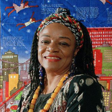 Photo of Faith Ringgold in front of one of her quilts. 