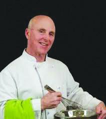 Image of Chef Rob wearing a white chef's coat, lime green hand towel over his arm with a bowl and whisk.