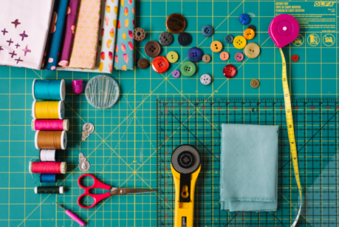 Image of sewing tools including buttons, spools of thread, tape measure, scissors and fabric. 